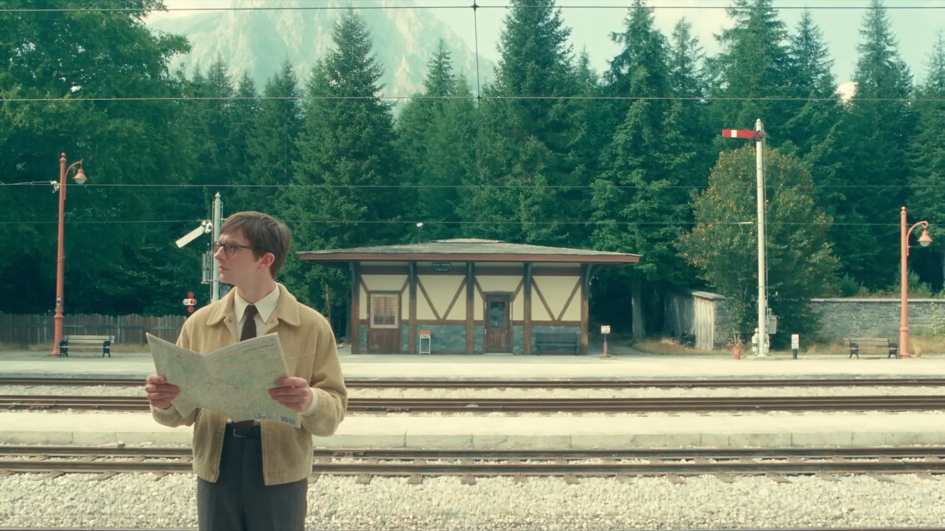 Still from Introducing Rocco Studio: a man reads a map on an alpine railway platform