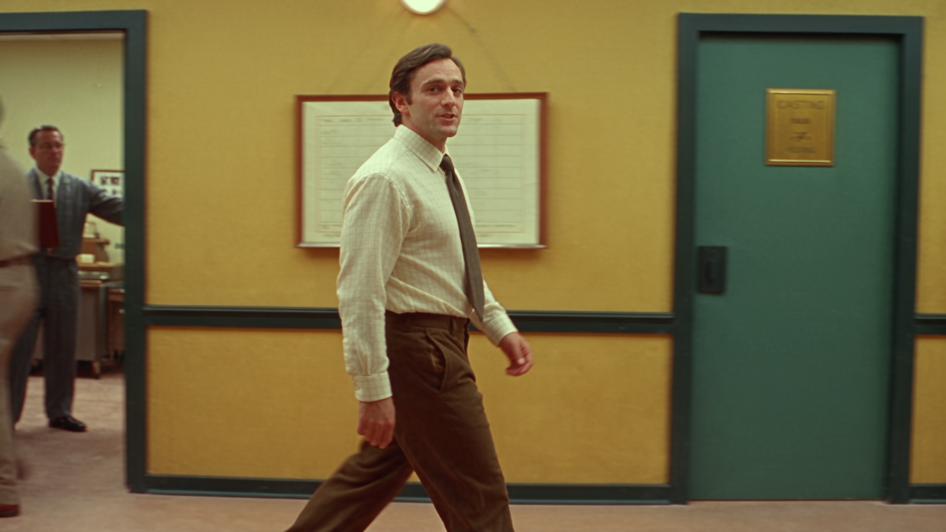 Still from Introducing Rocco Studio: a man walking a yellow corridor past a casting door