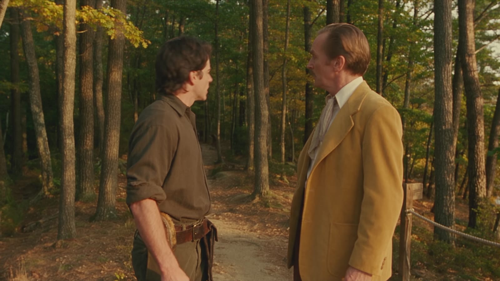 Still from Can You Swim?: two men mid-escape on a wooded clifftop trail at golden hour