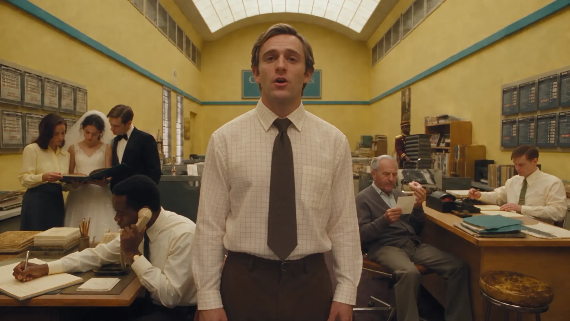 Still from Introducing Rocco Studio: a man addresses camera in a busy pastel office