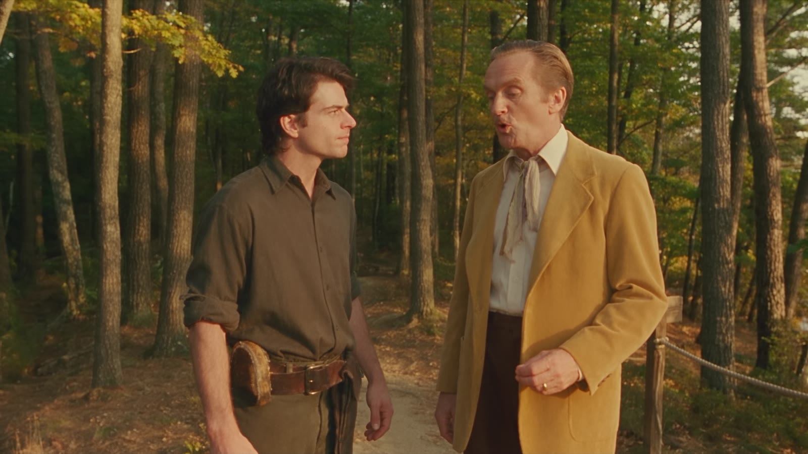 Still from Can You Swim?: the older man in a mustard jacket questions the younger man mid-flight